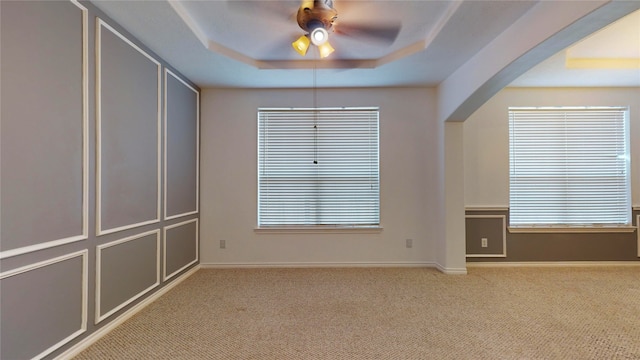 carpeted empty room featuring a wealth of natural light, ceiling fan, and a tray ceiling