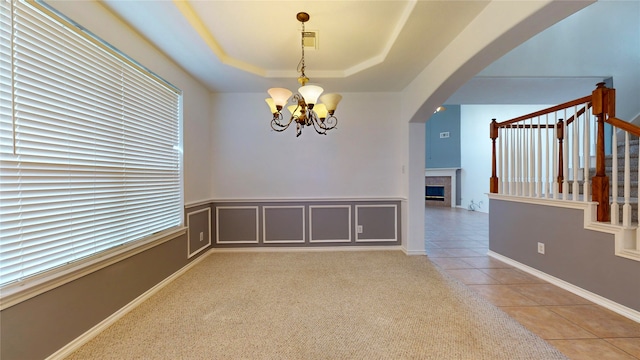 empty room with a tray ceiling, an inviting chandelier, light tile patterned floors, and a fireplace