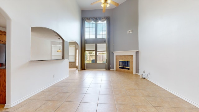 unfurnished living room with a towering ceiling, light tile patterned flooring, ceiling fan, and a tile fireplace