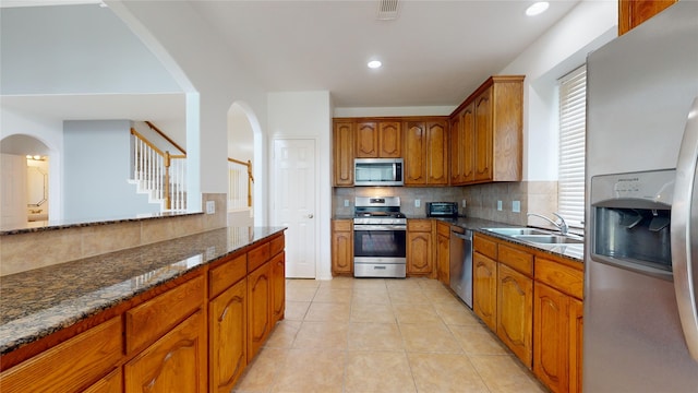 kitchen featuring light tile patterned flooring, sink, appliances with stainless steel finishes, tasteful backsplash, and dark stone countertops