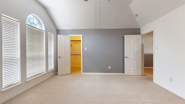 unfurnished bedroom with a spacious closet, lofted ceiling, light carpet, and a closet