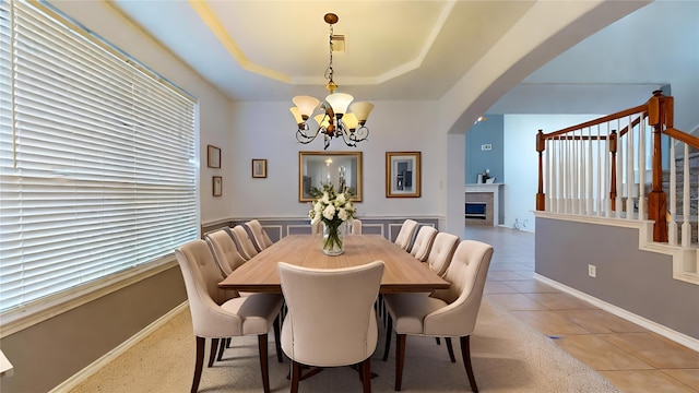 tiled dining space featuring a fireplace, a raised ceiling, and an inviting chandelier