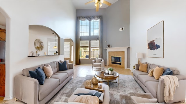 living room with a tiled fireplace, light tile patterned floors, a high ceiling, and ceiling fan