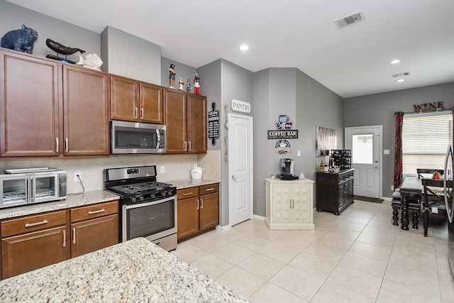 kitchen featuring stainless steel appliances, light tile patterned floors, backsplash, and light stone counters