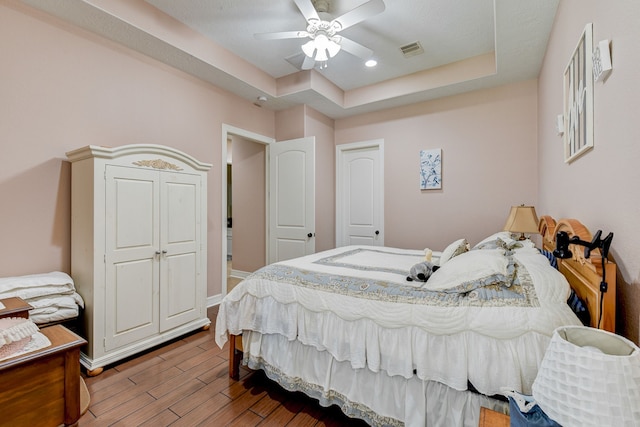 bedroom with hardwood / wood-style flooring, ceiling fan, and a tray ceiling