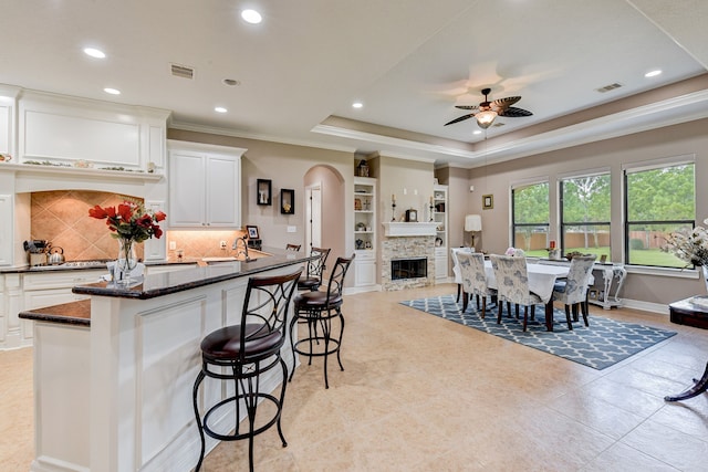 kitchen featuring tasteful backsplash, ceiling fan, dark stone countertops, a fireplace, and white cabinets