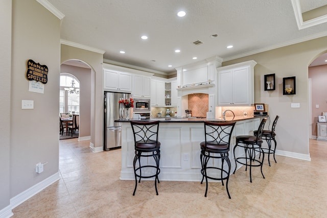 kitchen featuring crown molding, stainless steel appliances, white cabinetry, decorative backsplash, and a breakfast bar