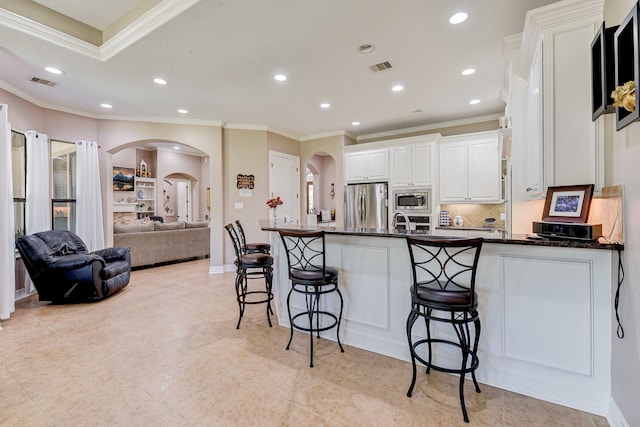 kitchen with a kitchen bar, kitchen peninsula, ornamental molding, white cabinetry, and appliances with stainless steel finishes