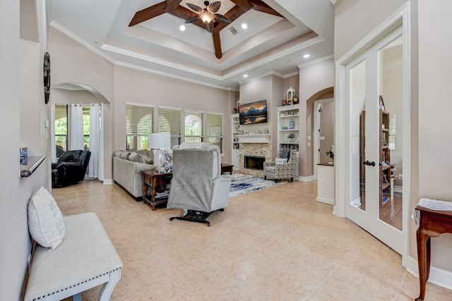 tiled bedroom with french doors, ornamental molding, a stone fireplace, a raised ceiling, and ceiling fan