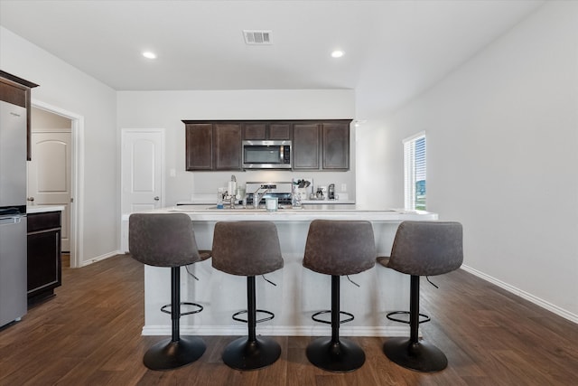 kitchen with dark hardwood / wood-style flooring, dark brown cabinetry, an island with sink, and stainless steel appliances