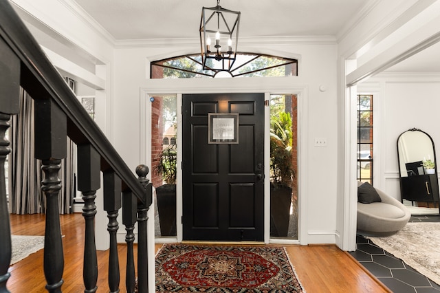 entrance foyer with a chandelier, wood-type flooring, vaulted ceiling, and ornamental molding