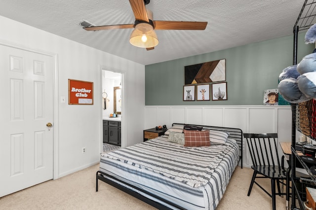 bedroom with a textured ceiling, ceiling fan, light carpet, and ensuite bath