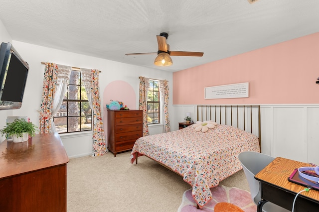 bedroom featuring a textured ceiling, light colored carpet, multiple windows, and ceiling fan