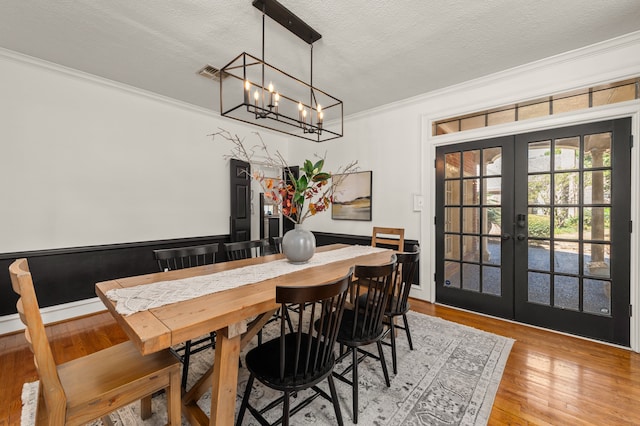 dining area with french doors, light wood-type flooring, ornamental molding, a textured ceiling, and a chandelier