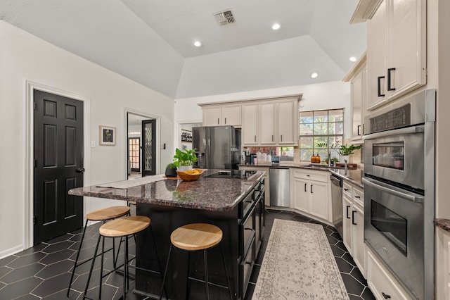 kitchen with dark stone countertops, a kitchen island, stainless steel appliances, and lofted ceiling