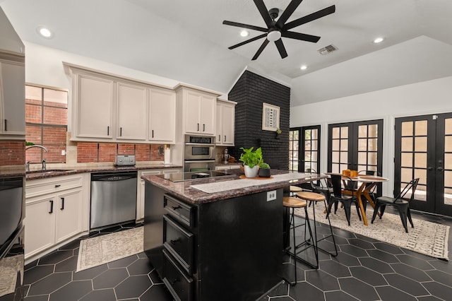 kitchen featuring french doors, a center island, dark stone counters, lofted ceiling, and appliances with stainless steel finishes