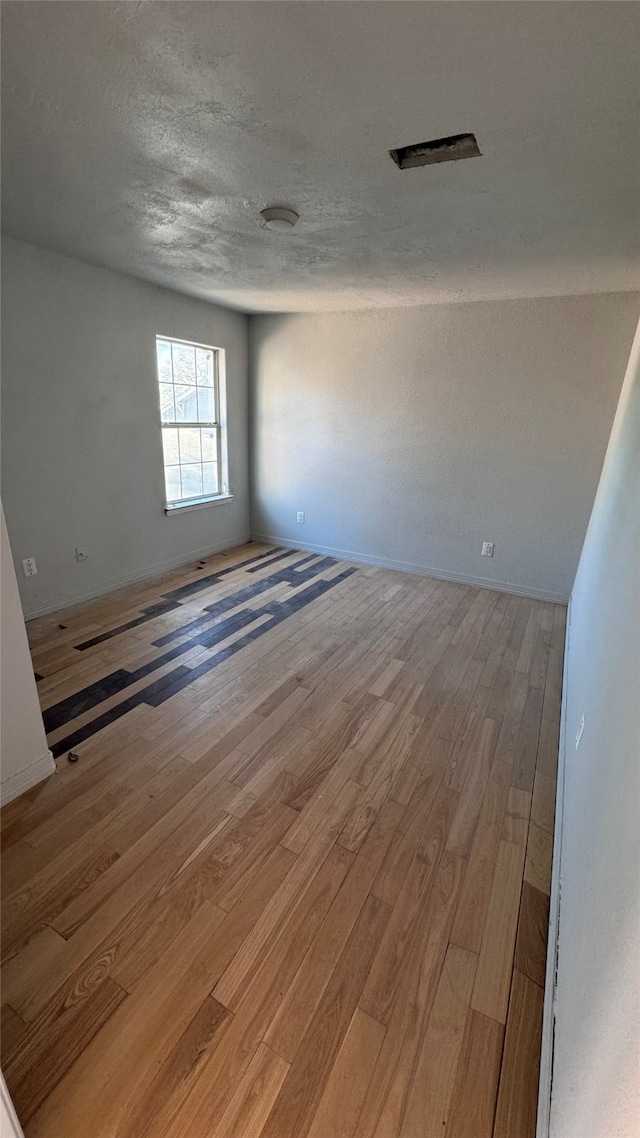 unfurnished room with a textured ceiling and light wood-type flooring