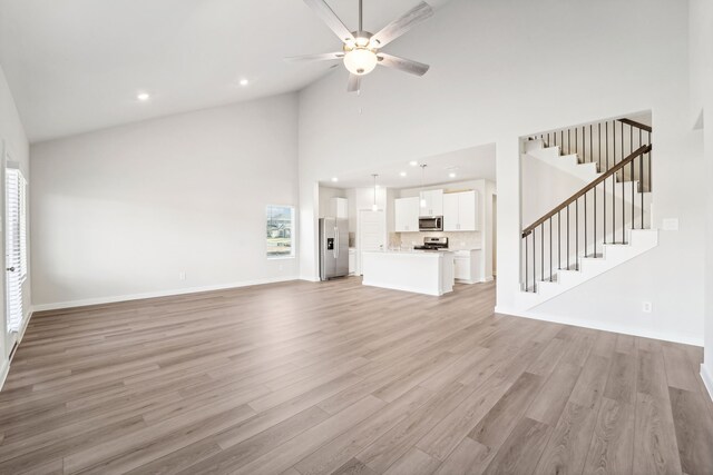 unfurnished living room featuring ceiling fan, high vaulted ceiling, and light wood-type flooring