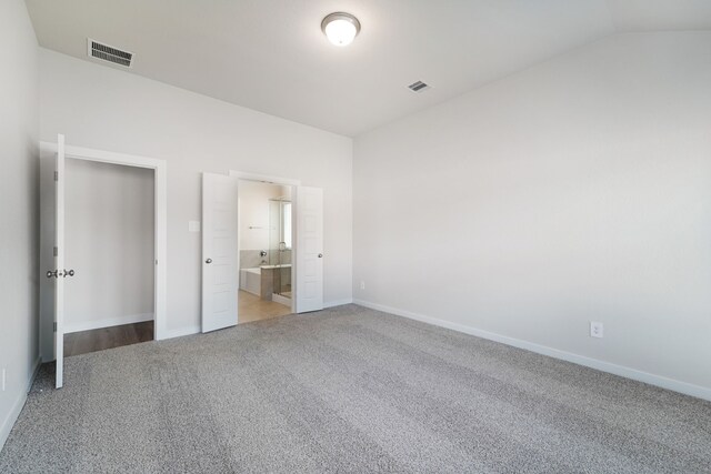 unfurnished bedroom featuring connected bathroom, light carpet, and lofted ceiling