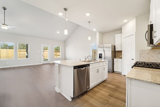 kitchen featuring light wood-type flooring, stainless steel appliances, white cabinetry, hanging light fixtures, and an island with sink