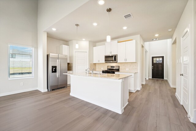 kitchen featuring white cabinets, appliances with stainless steel finishes, light hardwood / wood-style floors, and hanging light fixtures