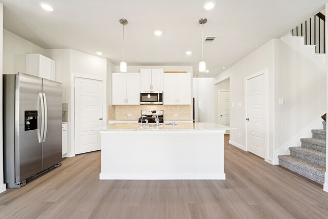 kitchen featuring stainless steel appliances, pendant lighting, light hardwood / wood-style floors, a center island with sink, and white cabinets