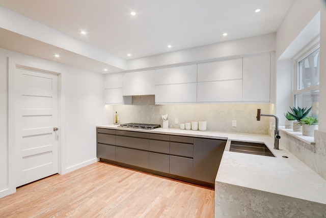 kitchen featuring sink, tasteful backsplash, light hardwood / wood-style floors, white cabinets, and stainless steel gas stovetop