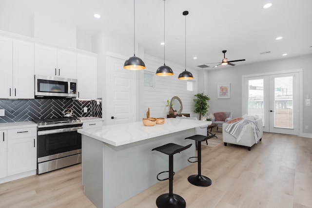 kitchen featuring appliances with stainless steel finishes, light wood-type flooring, pendant lighting, white cabinets, and a kitchen island