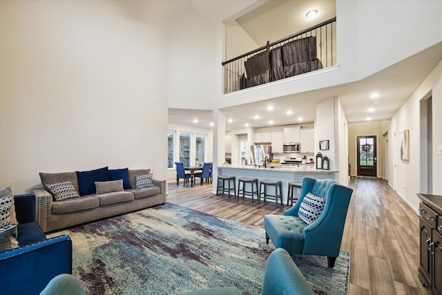 living room featuring a high ceiling, sink, and light hardwood / wood-style flooring