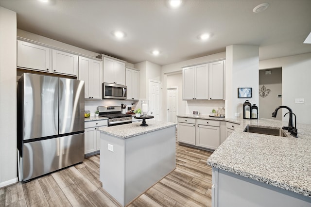 kitchen with stainless steel appliances, kitchen peninsula, sink, white cabinetry, and light wood-type flooring