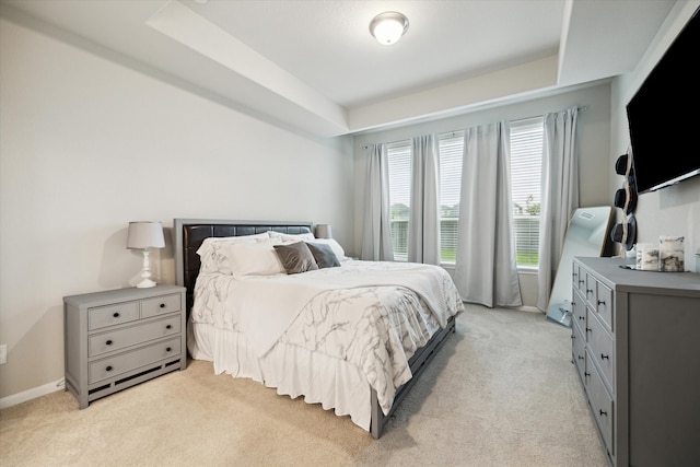 bedroom with light colored carpet and a raised ceiling