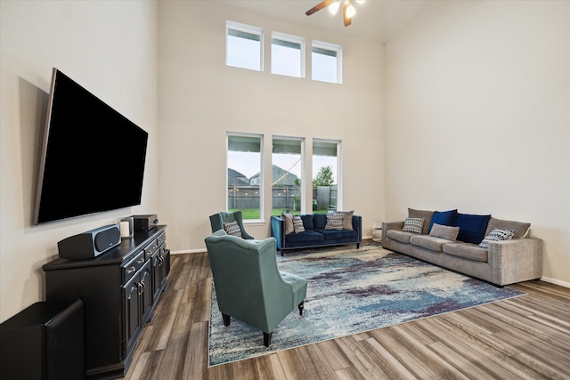 living room featuring ceiling fan, hardwood / wood-style flooring, a high ceiling, and a healthy amount of sunlight