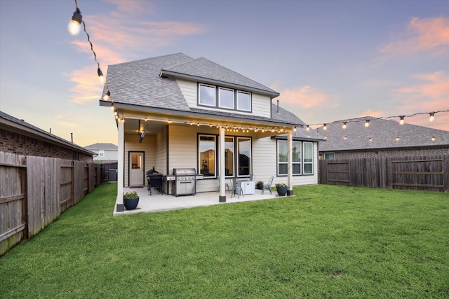 back house at dusk with a lawn and a patio area