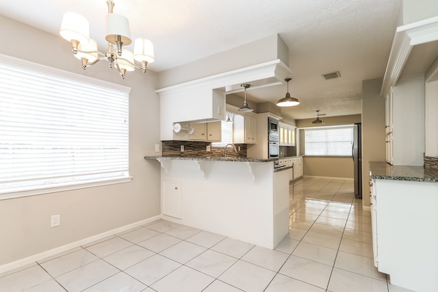 kitchen featuring backsplash, pendant lighting, white cabinets, kitchen peninsula, and a breakfast bar area