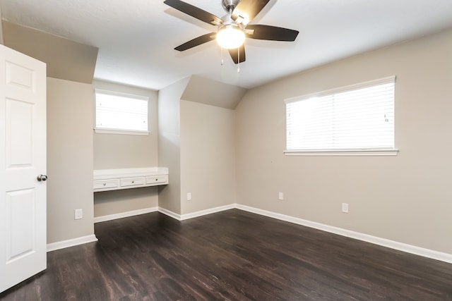 unfurnished bedroom featuring dark hardwood / wood-style flooring, vaulted ceiling, built in desk, and ceiling fan