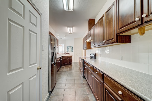 kitchen with appliances with stainless steel finishes, a textured ceiling, light tile patterned floors, sink, and decorative backsplash