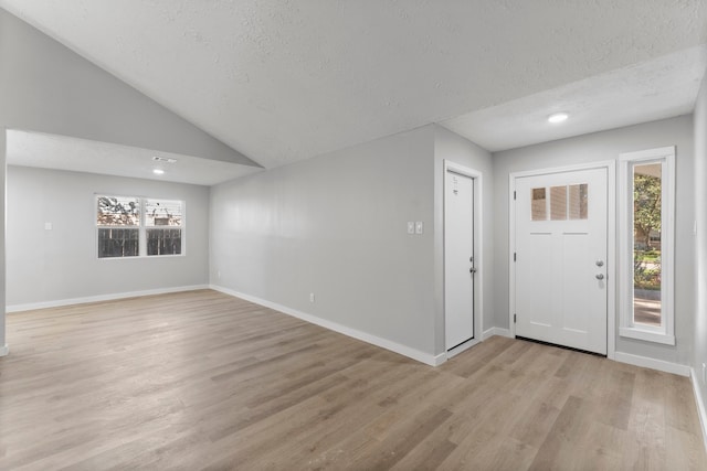 foyer featuring a textured ceiling, light wood-type flooring, plenty of natural light, and lofted ceiling