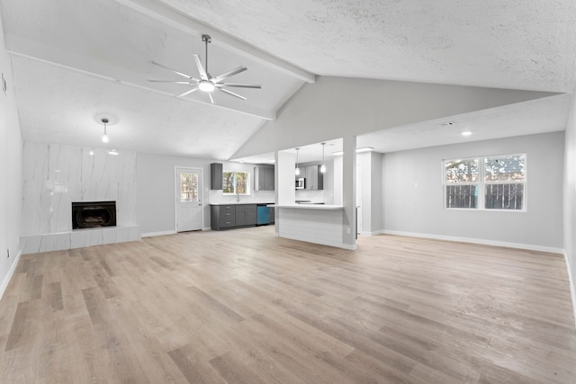 unfurnished living room featuring a textured ceiling, lofted ceiling with beams, light hardwood / wood-style flooring, and a tiled fireplace