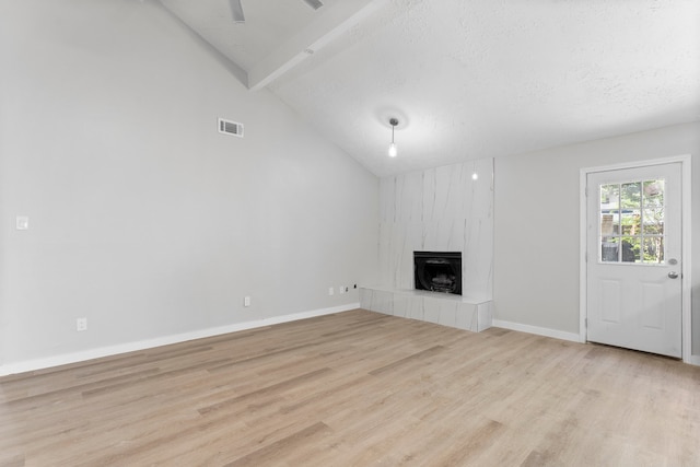 unfurnished living room featuring a textured ceiling, light wood-type flooring, high vaulted ceiling, and a tiled fireplace