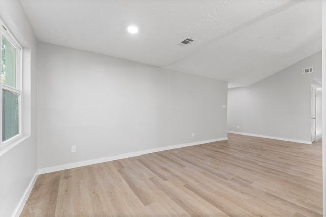 unfurnished room with a textured ceiling, vaulted ceiling, and light hardwood / wood-style flooring