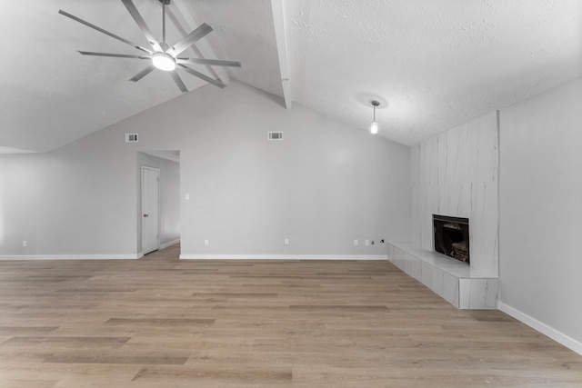 unfurnished living room featuring light wood-type flooring, a textured ceiling, ceiling fan, a tile fireplace, and vaulted ceiling with beams