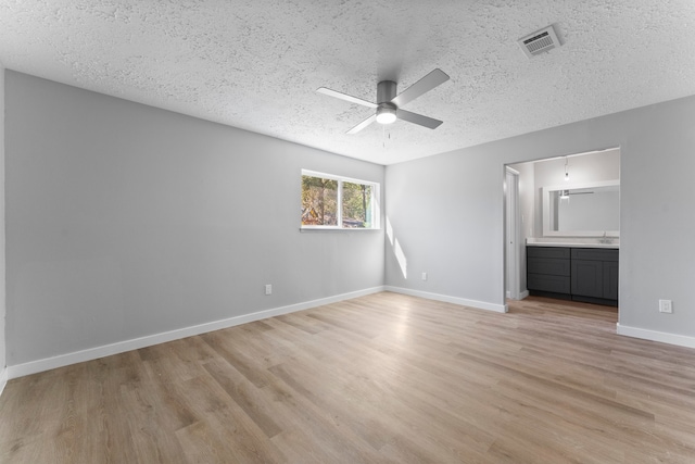 unfurnished bedroom featuring light wood-type flooring, a textured ceiling, connected bathroom, and ceiling fan