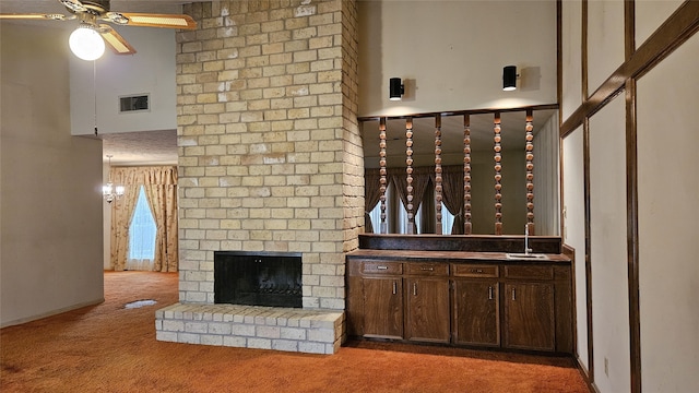 unfurnished living room with carpet flooring, a brick fireplace, ceiling fan, sink, and a high ceiling