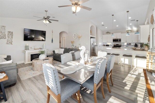 1286 Lagoon Dr, Crystal Beach, TX 77650 - dining space with arched walkways, ceiling fan, light wood-style floors, high vaulted ceiling, and a fireplace