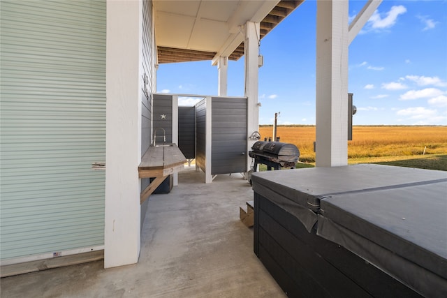 view of patio / terrace with a hot tub, a rural view, and a grill