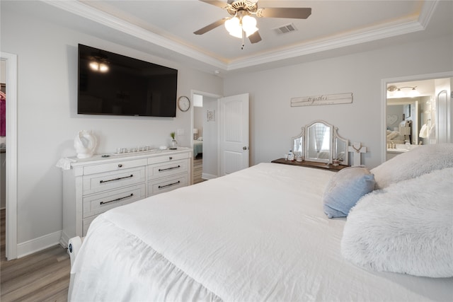 bedroom with ornamental molding, ensuite bath, a raised ceiling, ceiling fan, and light hardwood / wood-style flooring