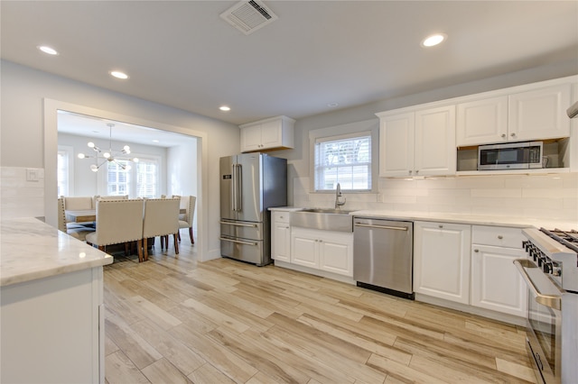 kitchen with white cabinets, light wood-type flooring, premium appliances, and a healthy amount of sunlight