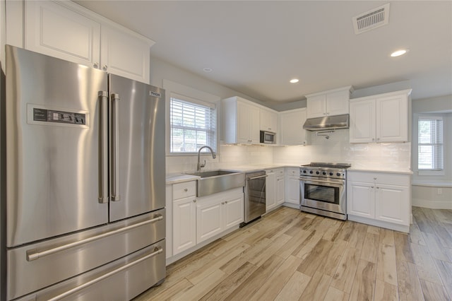 kitchen with white cabinetry, plenty of natural light, premium appliances, and light hardwood / wood-style floors