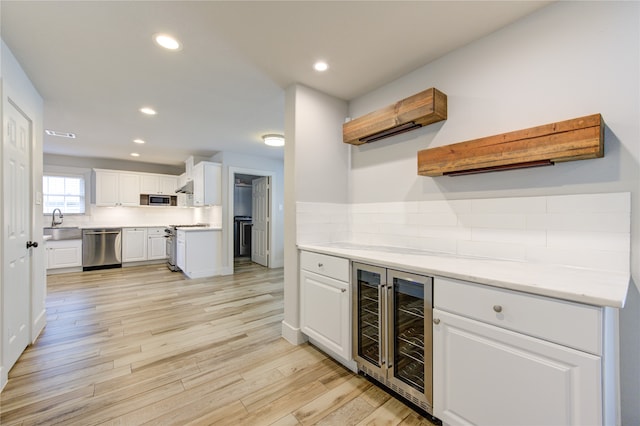 kitchen with appliances with stainless steel finishes, light wood-type flooring, beverage cooler, white cabinets, and an AC wall unit