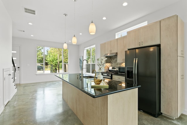 kitchen with a center island with sink, appliances with stainless steel finishes, light brown cabinets, decorative light fixtures, and decorative backsplash